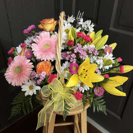Basket arrangement of pink gerberas, yellow lilies, and mixed daisies with a yellow bow