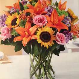 Mixed bouquet of sunflowers, orange lilies, and pink roses in a glass vase