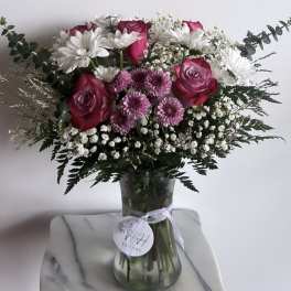 Bouquet of pink roses, white daisies, and purple mums in a glass vase
