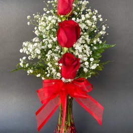 Three red roses in a clear vase with baby's breath and a red ribbon