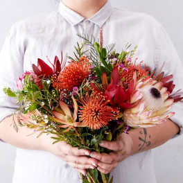 Person holding a bouquet of red and orange tropical flowers