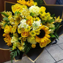 Yellow bouquet with roses, sunflowers, and white blooms wrapped in black paper