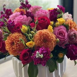 Mixed bouquet of roses, dahlias, and purple blooms in a white vase