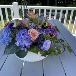 Low floral arrangement with pink roses and purple hydrangeas in a white bowl