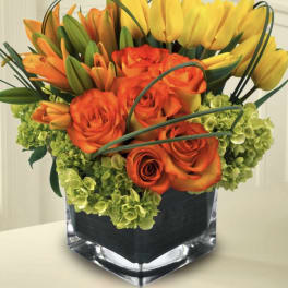 Orange roses and yellow tulips arranged in a square glass vase