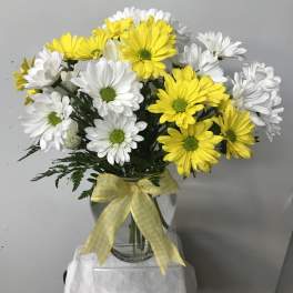 Yellow and white daisy bouquet in a glass vase with a gingham ribbon