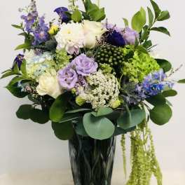 Mixed bouquet of purple, white, and green flowers in a tall dark vase