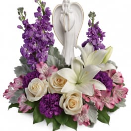 Purple and pink floral arrangement with white lilies and roses around an angel figurine