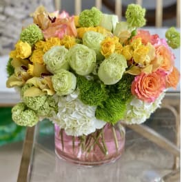 Bouquet of yellow, peach, and green flowers in a pink glass vase