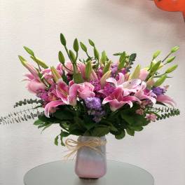 Pink lilies and purple flowers in a frosted vase with a bow