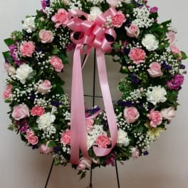 Heart-shaped floral wreath with pink ribbon on a stand