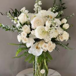 White roses and orchids arranged in a tall glass vase
