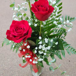 Three red roses in a clear vase with white baby's breath