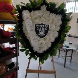 Heart-shaped white floral tribute on an easel with a Raiders emblem and ribbon