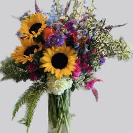 Bouquet of sunflowers, roses, and mixed blooms in a clear glass vase