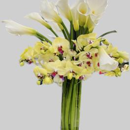 Yellow orchids and white calla lilies in a tall glass vase