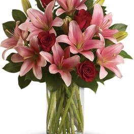 Pink lilies and red roses arranged in a clear glass vase