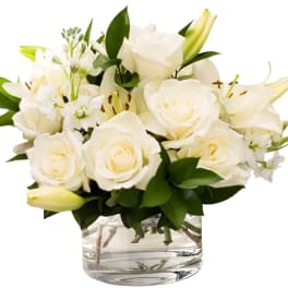 White roses and lilies arranged in a clear glass vase