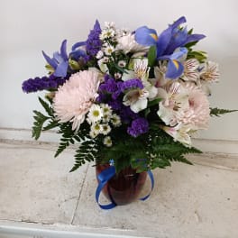 Purple and white mixed bouquet in a red glass vase with blue ribbon
