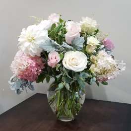 Arrangement of white and blush roses, hydrangeas, and a dahlia in a clear glass vase on a dark table