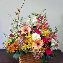 Colorful mixed flower basket with gerbera daisies, roses, snapdragons, and mums in warm tones.