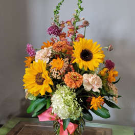 Tall mixed arrangement with sunflowers, hydrangea, and assorted orange and peach blooms in a glass vase.