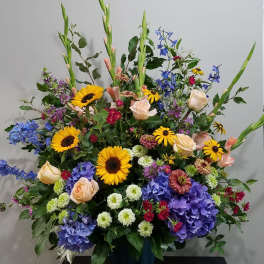Large mixed arrangement with sunflowers, roses, hydrangeas, and assorted blooms in a dark container