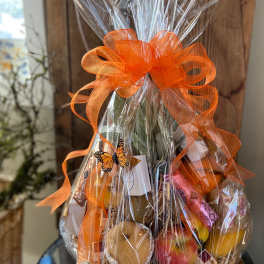 Cellophane-wrapped fruit and snack gift basket with a large orange bow and butterfly accent.