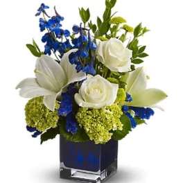 White lilies and roses with blue flowers in a square glass vase