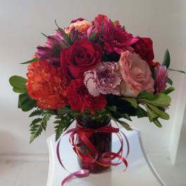 Bouquet of red, pink, and orange flowers in a glass vase with ribbon