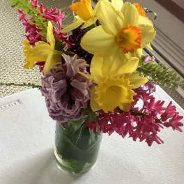 Bouquet of yellow daffodils, pink hyacinths, and purple blooms in a glass vase