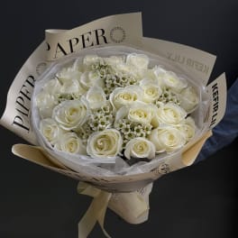 Bouquet of white roses wrapped in cream paper with a ribbon
