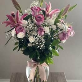 Pink lilies and roses in a glass vase with a ribbon