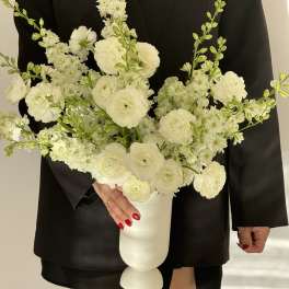 White floral arrangement in a white pedestal vase held against a black outfit