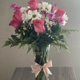 Pink roses and white daisies in a clear glass vase with a pink ribbon