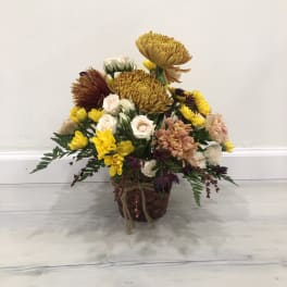 Mixed bouquet of yellow, white, pink, and burgundy flowers in a woven basket