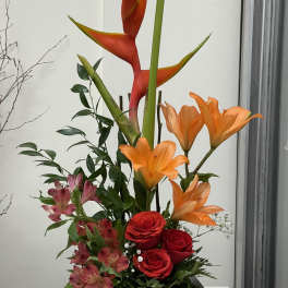 Tropical arrangement with orange heliconia, red roses, and pink alstroemeria in a dark vase
