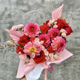 Pink and red bouquet with roses and dahlias wrapped in pastel paper
