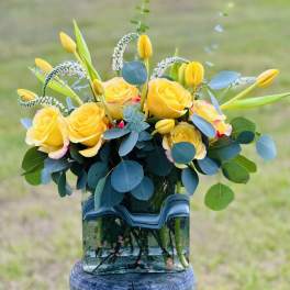 Yellow roses and tulips arranged in a glass vase