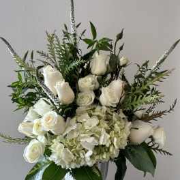 White roses and hydrangeas in a clear vase with tall greenery