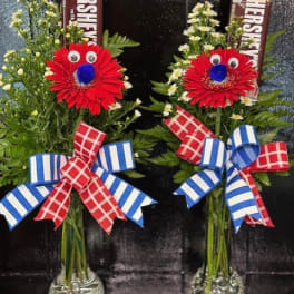 Two floral arrangements with red daisies and Hershey's bars in glass vases