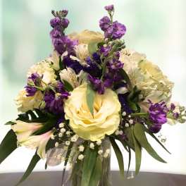 Bouquet of pale yellow roses and purple flowers in a glass vase
