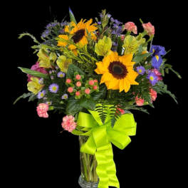 Bouquet of sunflowers, alstroemeria, and purple daisies in a glass vase with a lime ribbon