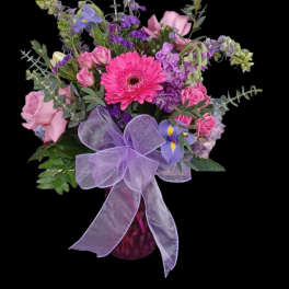 Pink and purple mixed bouquet in a glass vase with a lavender bow