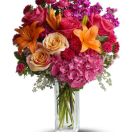 Mixed bouquet of pink roses, orange lilies, and hydrangeas in a glass vase