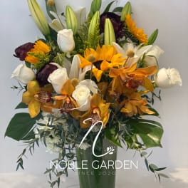 Mixed bouquet of lilies, roses, orchids, and sunflowers in a glass vase