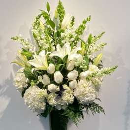 Tall white floral arrangement in a glass vase with lilies and hydrangeas