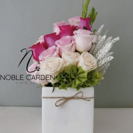 Pink and white roses arranged in a white box with twine
