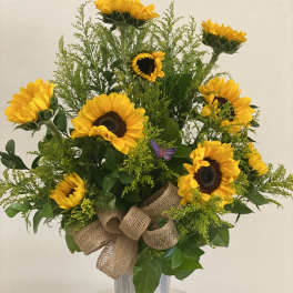 Sunflower arrangement in a tall silver vase with a burlap bow