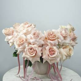 Blush pink roses arranged in a white vase with pink ribbons